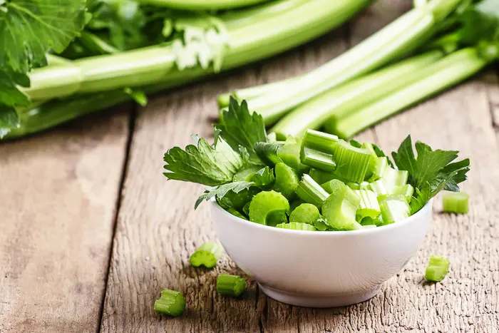 celery stalks chopped in a white bowl sitting on a wooden table
