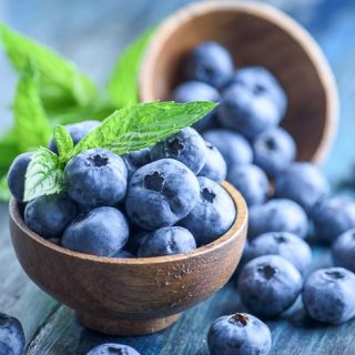 fresh blueberries in wooden bowl with blue background