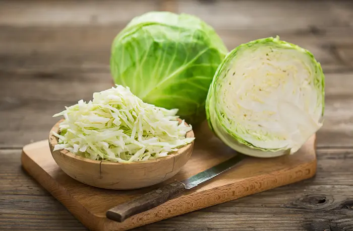 cabbage cut in half on cutting board with bowl of shredded cabbage on side