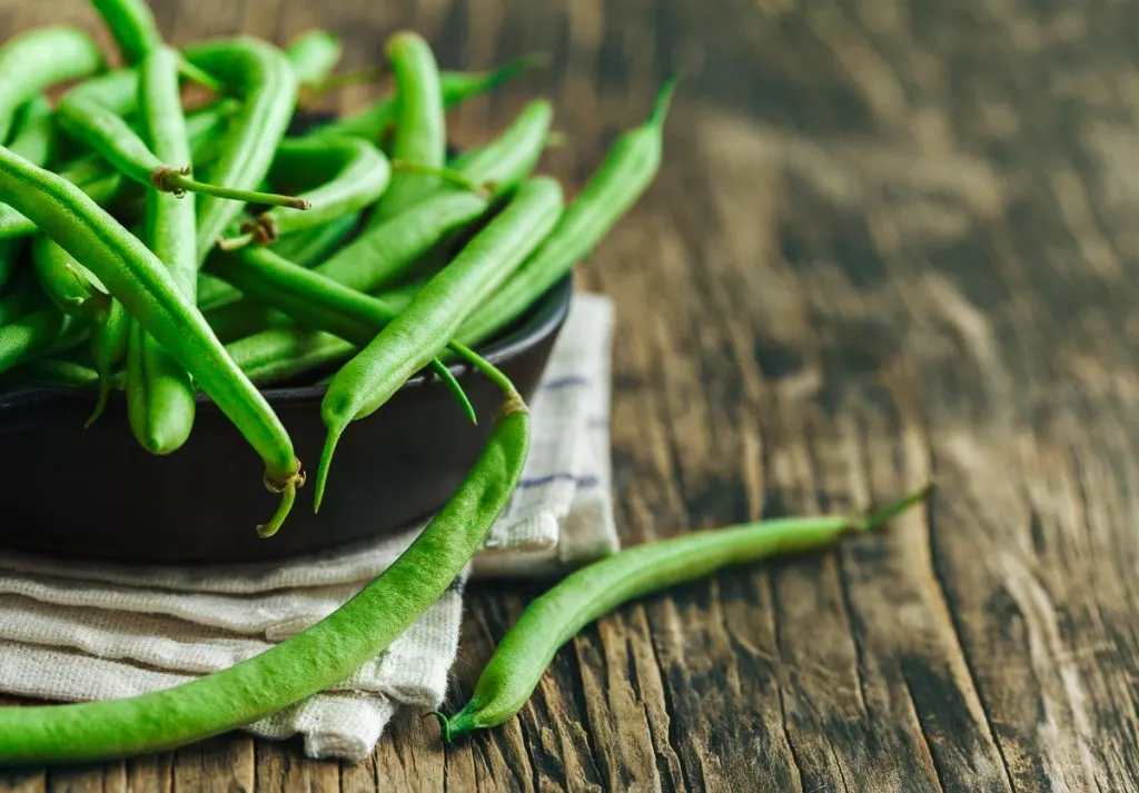 fresh raw green beans in black bowl sitting on wooden table