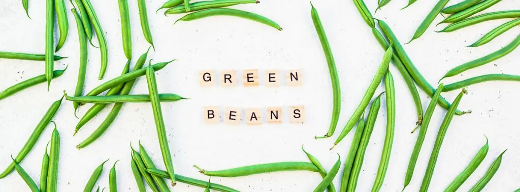 fresh raw green beans on white background with scrabble letters spelling out green beans