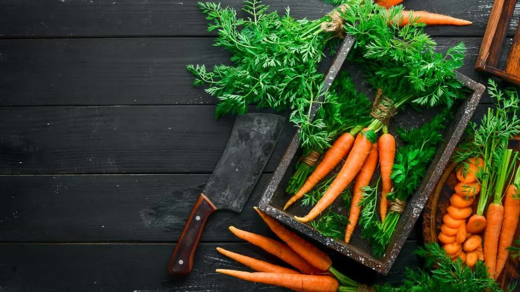 whole orange carrots with green carrot tops on black wooden table